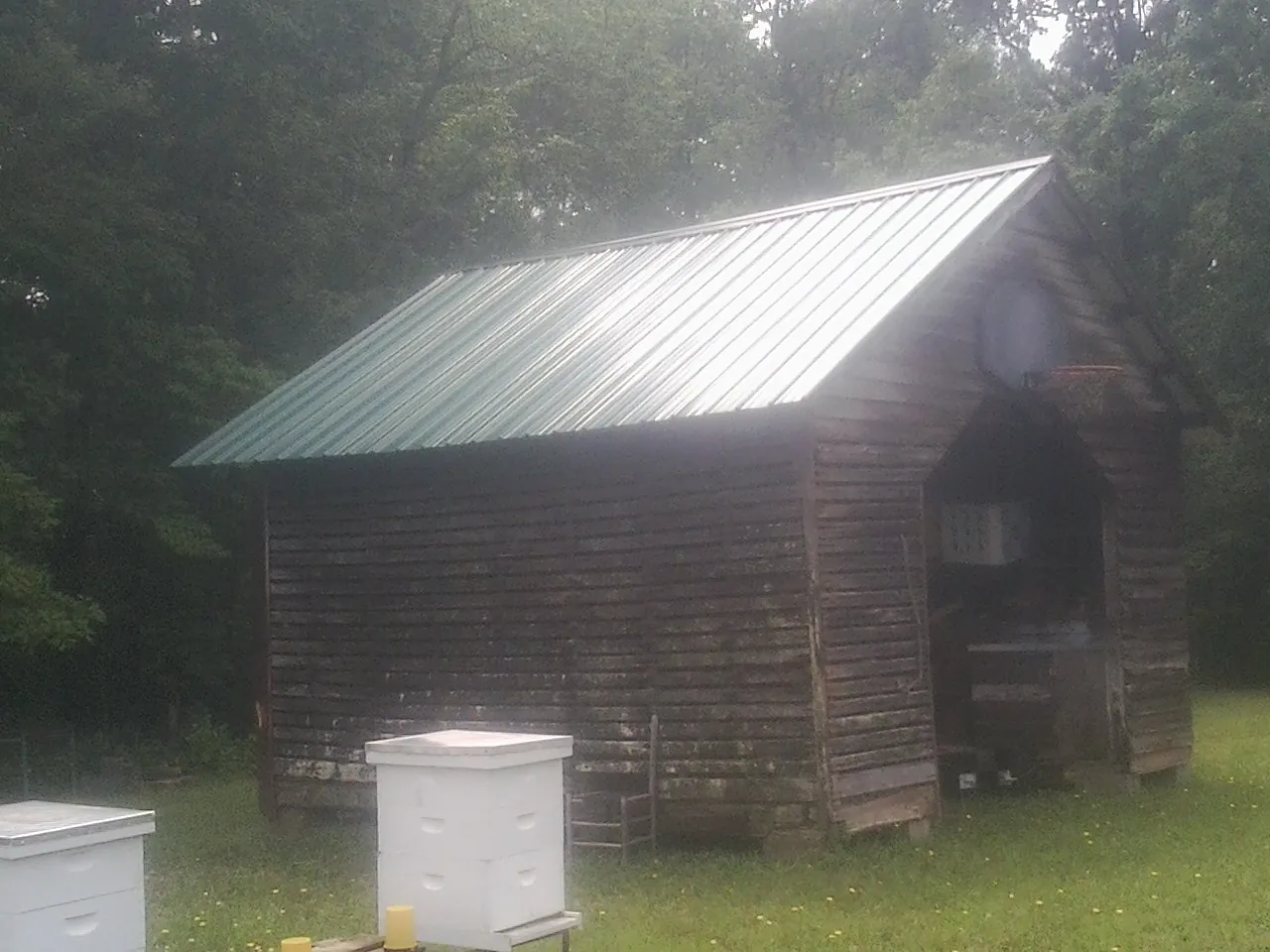Green metal roof on a weathered barn beside stacked beehives in Butler